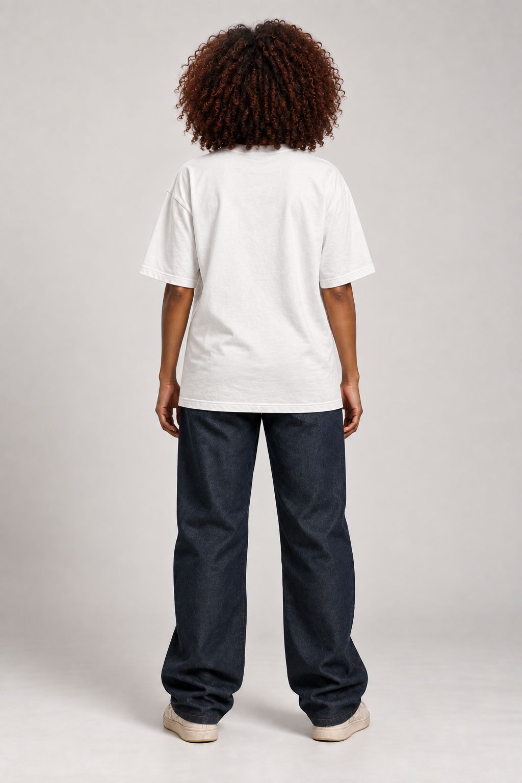 Rear view of Dawn wearing the white ISSUE #1 SKULL oversized T-shirt, showing its relaxed fit with dark trousers.