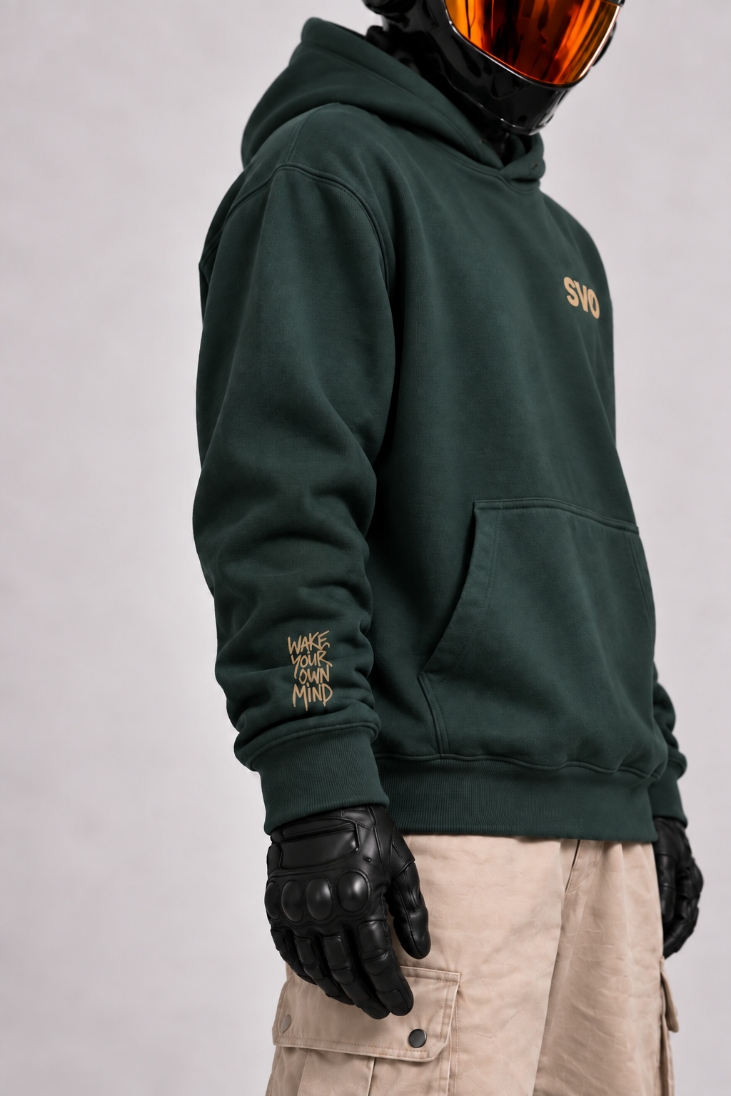 Close-up of a helmeted character wearing the pine green SVO hoodie, showing the relaxed fit, chest logo and gold sleeve detail.