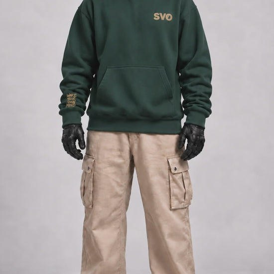 Front view of SVO wearing the pine green SVO oversized hoodie with beige cargo trousers.